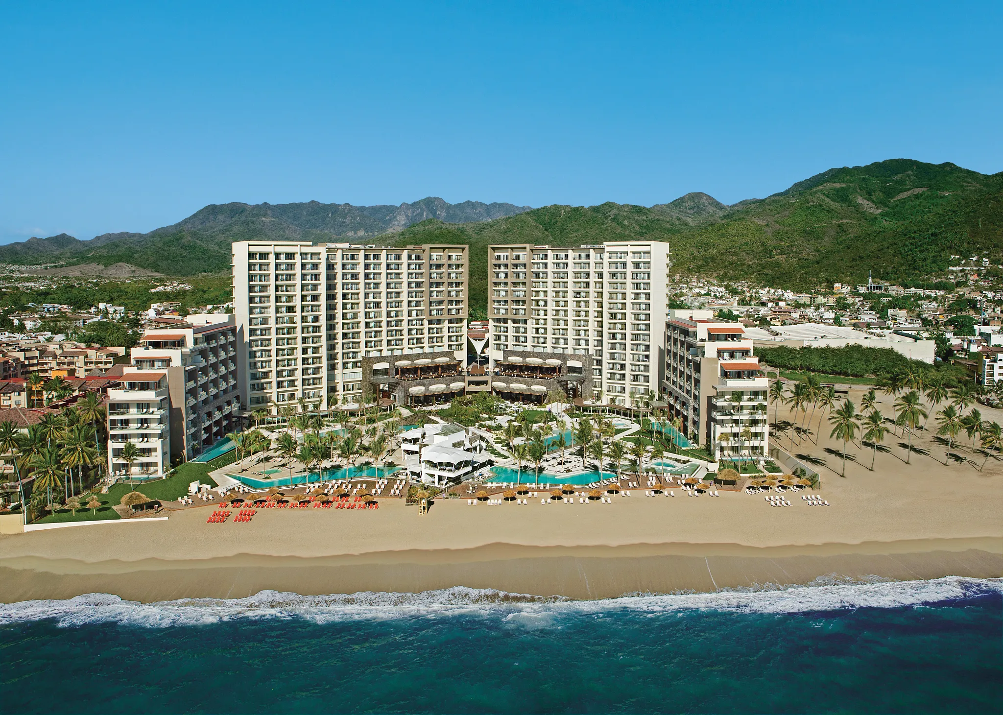 Aerial view of Dreams Vallarta Bay Resort & Spa beachfront property with pools and mountains in Puerto Vallarta.