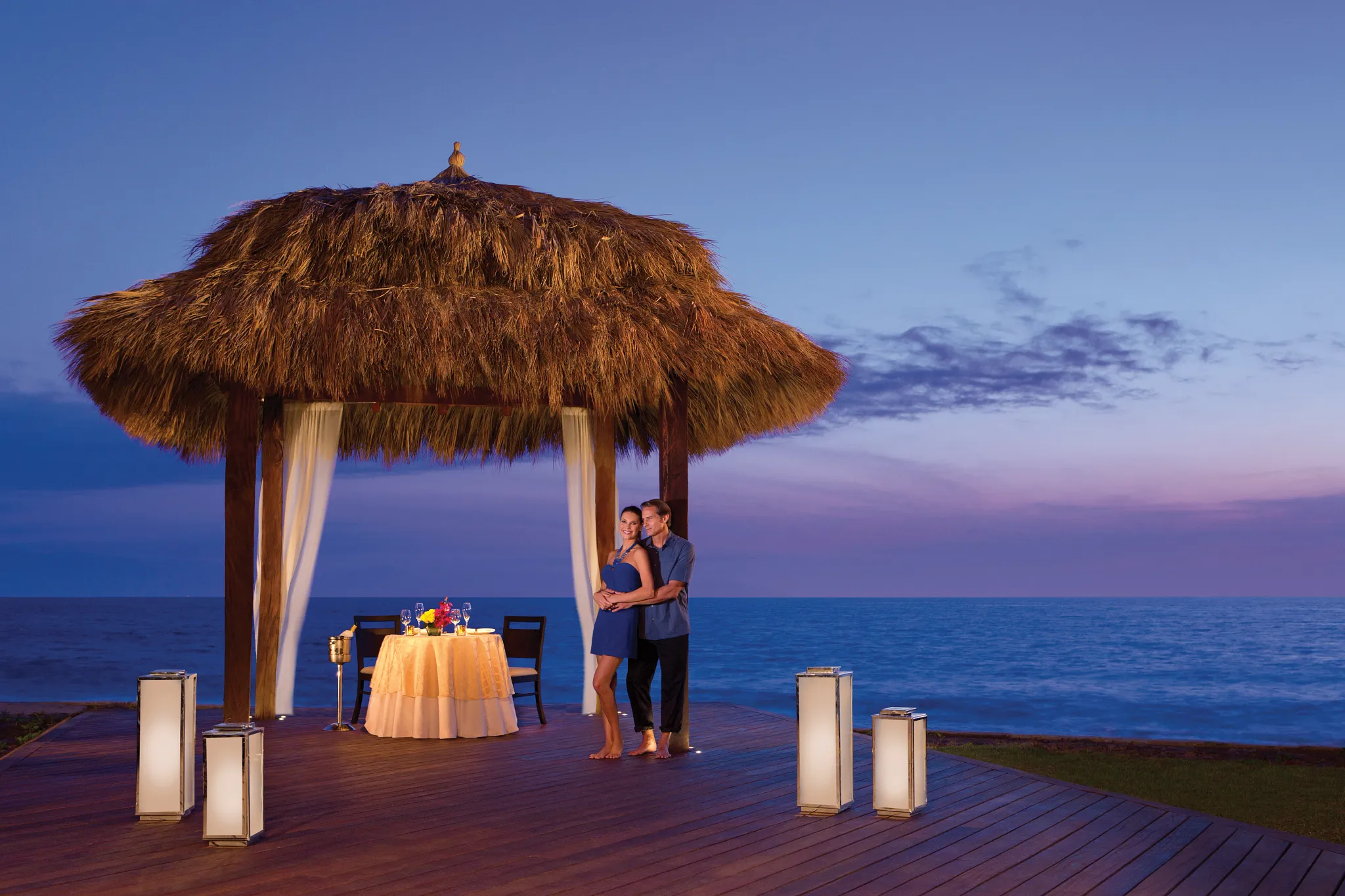 Couple enjoying a private romantic dinner under a thatched palapa overlooking the ocean at Dreams Vallarta Bay Resort & Spa.
